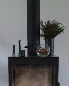 fireplace with a vase full of dry and evergreen brunches, three candles and glass vase with walnuts